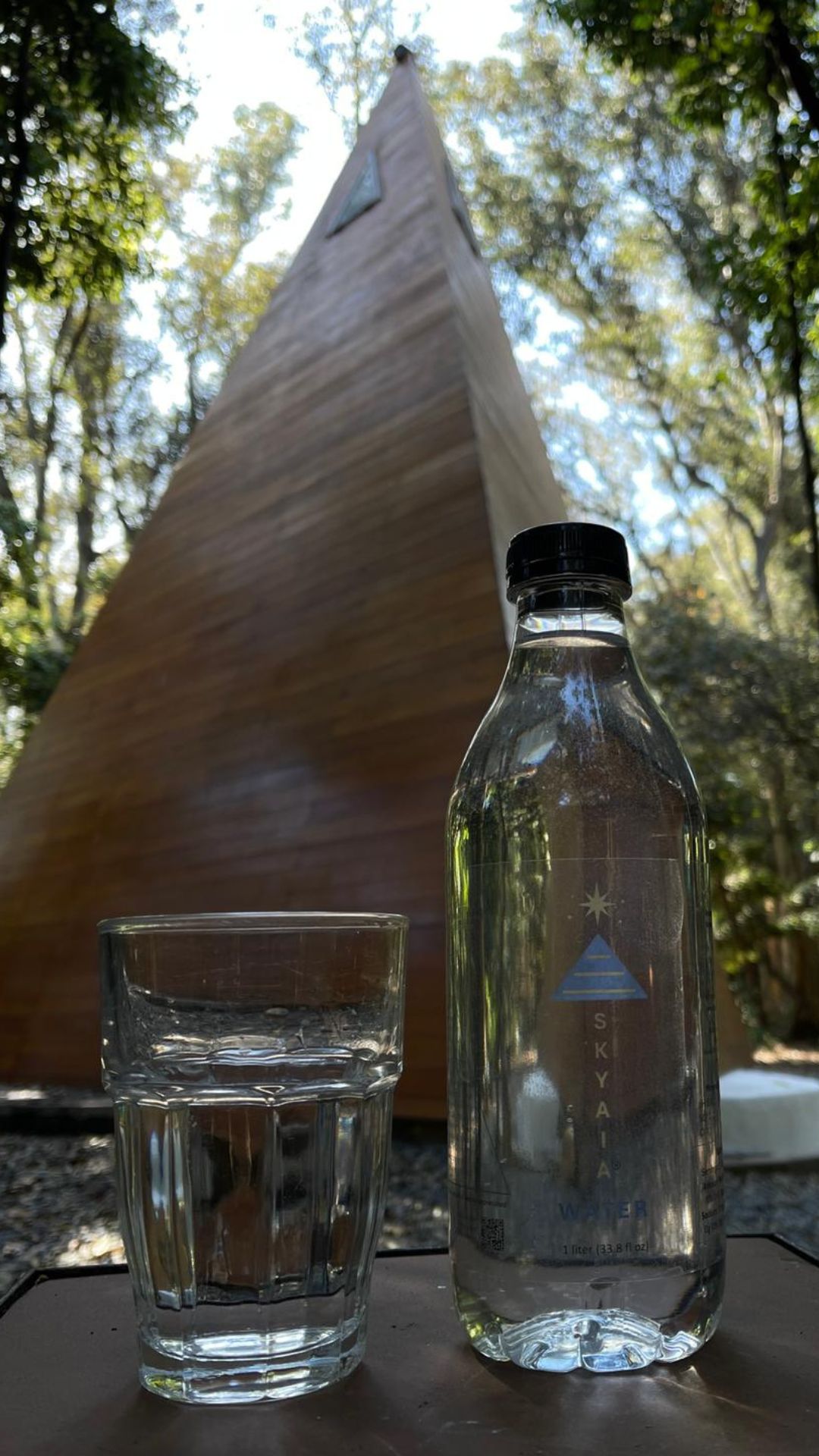 Click to view larger image Skyaia Water® bottle and glass with wooden pyramid structure in natural forest setting